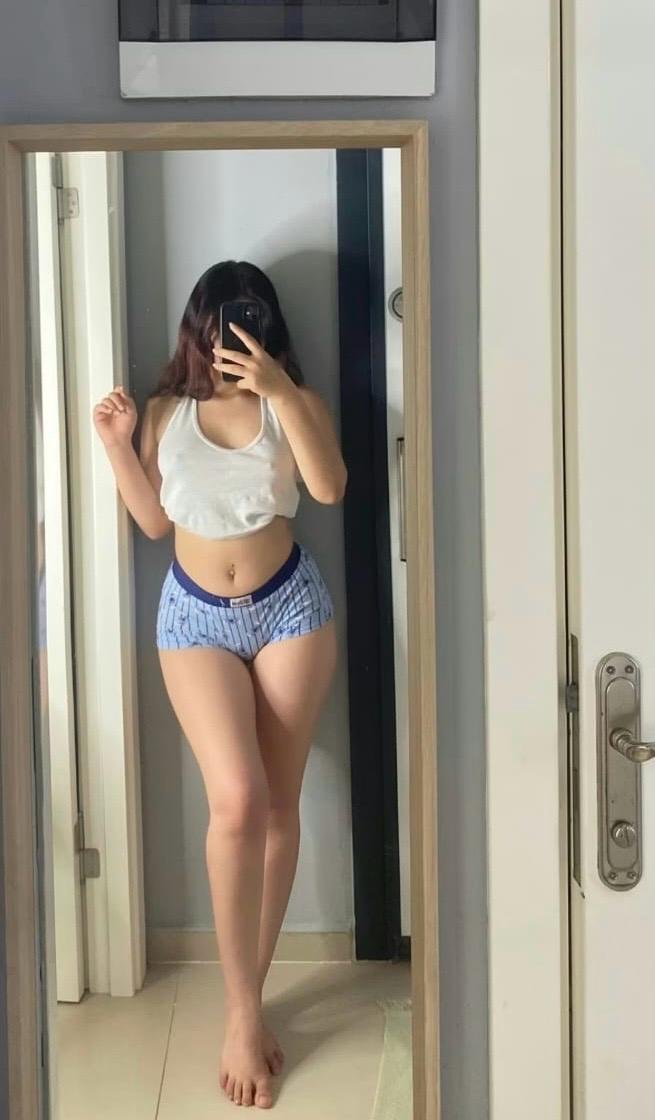 Woman taking a mirror selfie in a doorway, wearing a white crop top and blue striped shorts, barefoot.