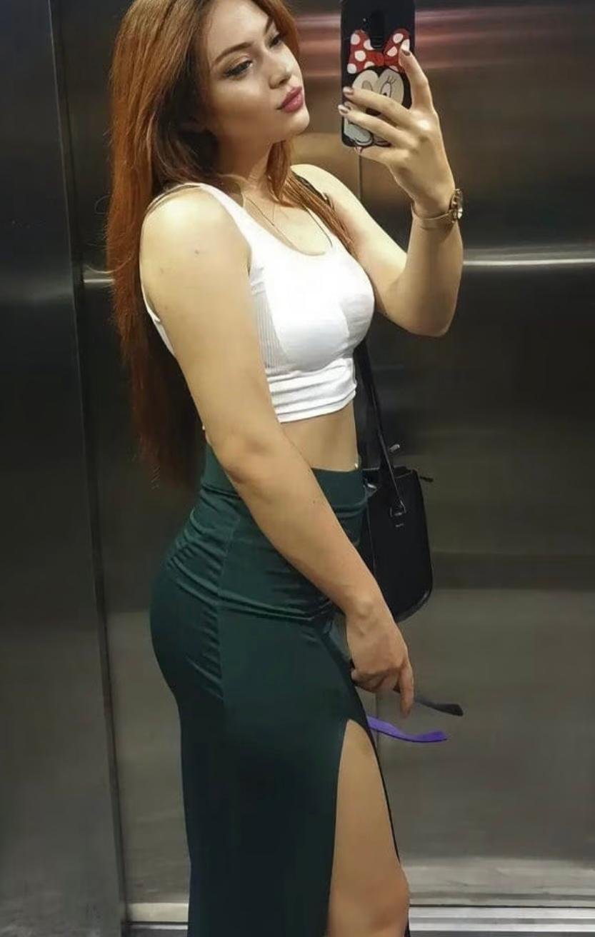 Woman in a white crop top and dark green high-slit skirt taking a mirror selfie in an elevator, Minnie Mouse phone case visible.